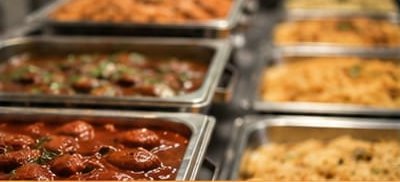 Trays of brinjal curry and side dishes on the counter